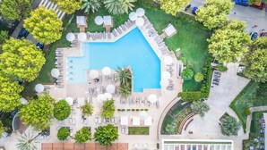 An aerial view of a resort with a central swimming pool, sun loungers, umbrellas, and surrounding greenery. - Canyamel Park Hotel & Spa - Adults Only (Capdepera)