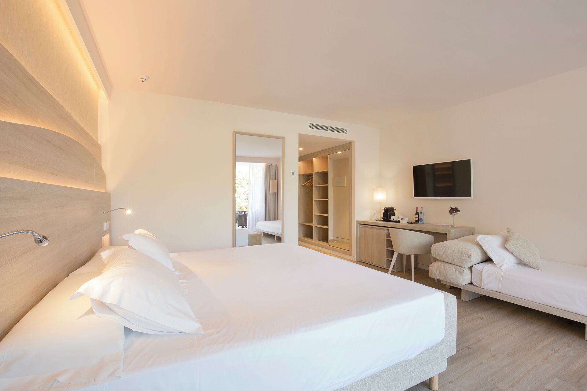 A modern hotel room with a large bed, a desk with a chair, a sofa, and a TV mounted on the wall.