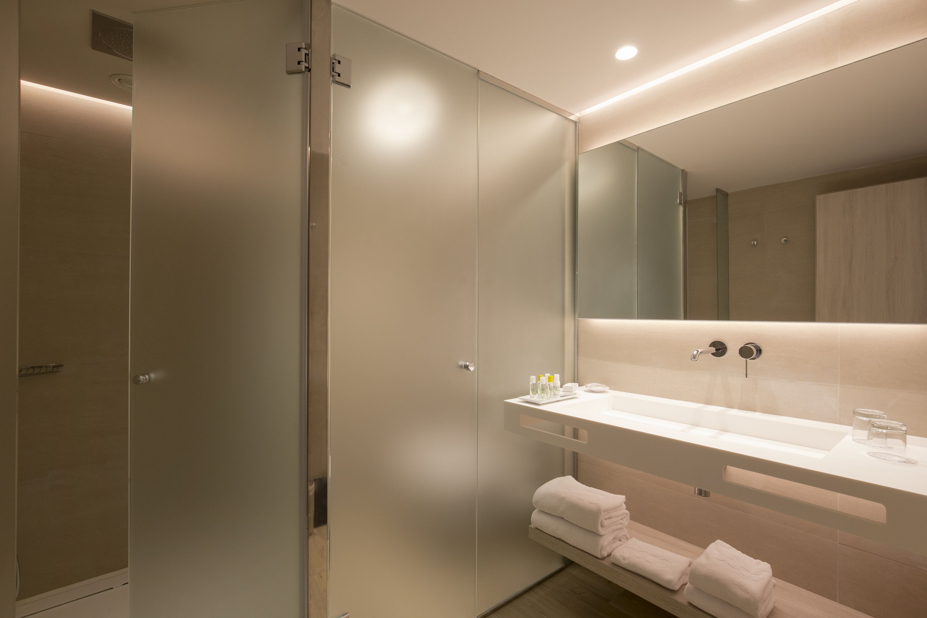 Un baño moderno con un espejo grande, un lavamanos blanco y toallas dobladas con cuidado.