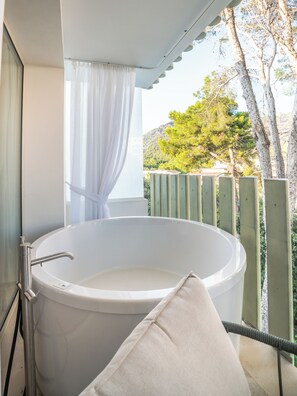 A modern bathroom with a freestanding bathtub, a shower curtain, and a view of a green landscape with trees and hills. - Canyamel Park Hotel & Spa - Adults Only (Capdepera)