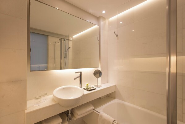 Un baño moderno con lavamanos blanco, espejo y ducha con cerramiento de vidrio.