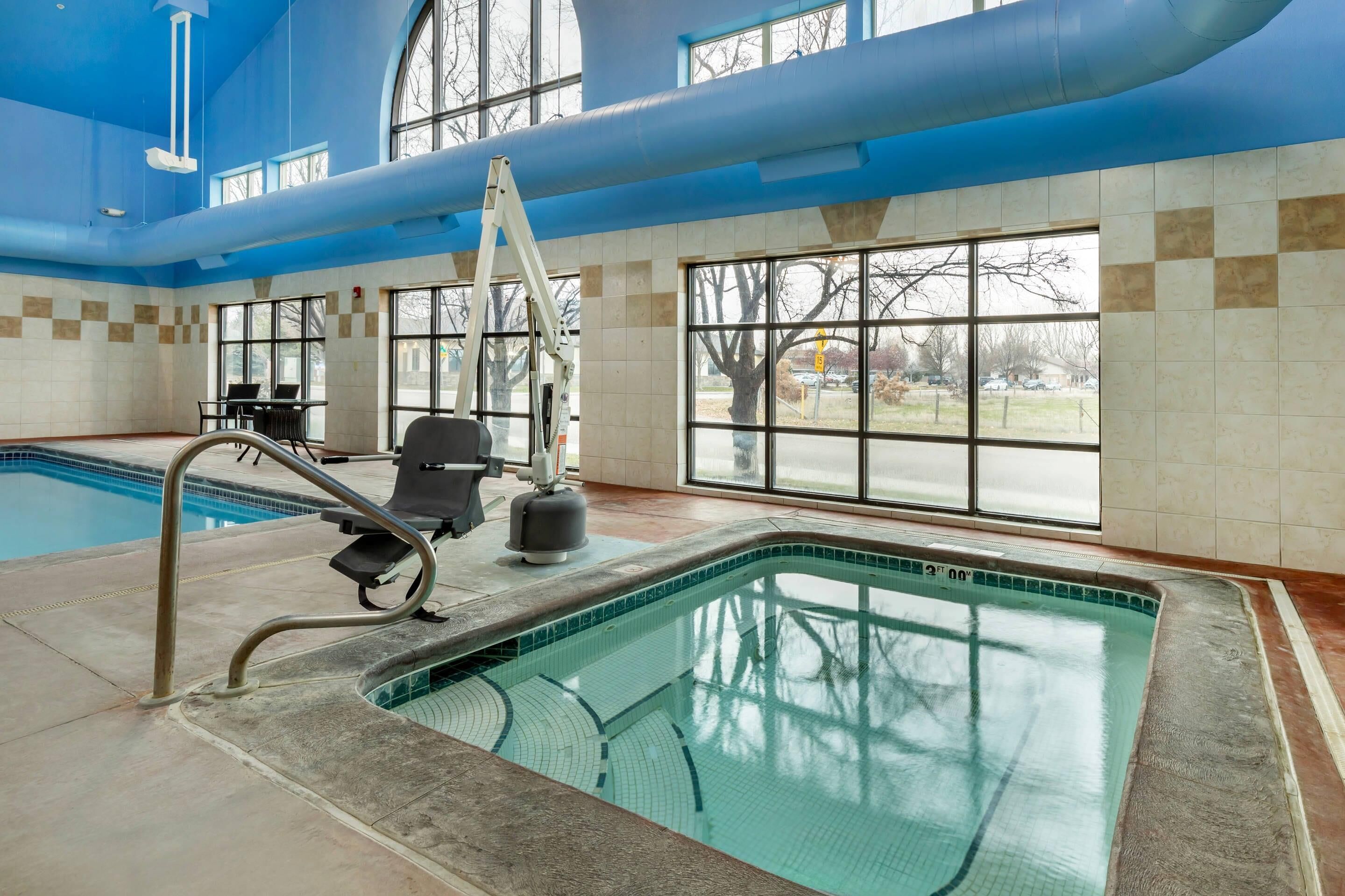 Une piscine intérieure avec des parois en verre transparent, une échelle et un poste de surveillance pour le sauveteur.