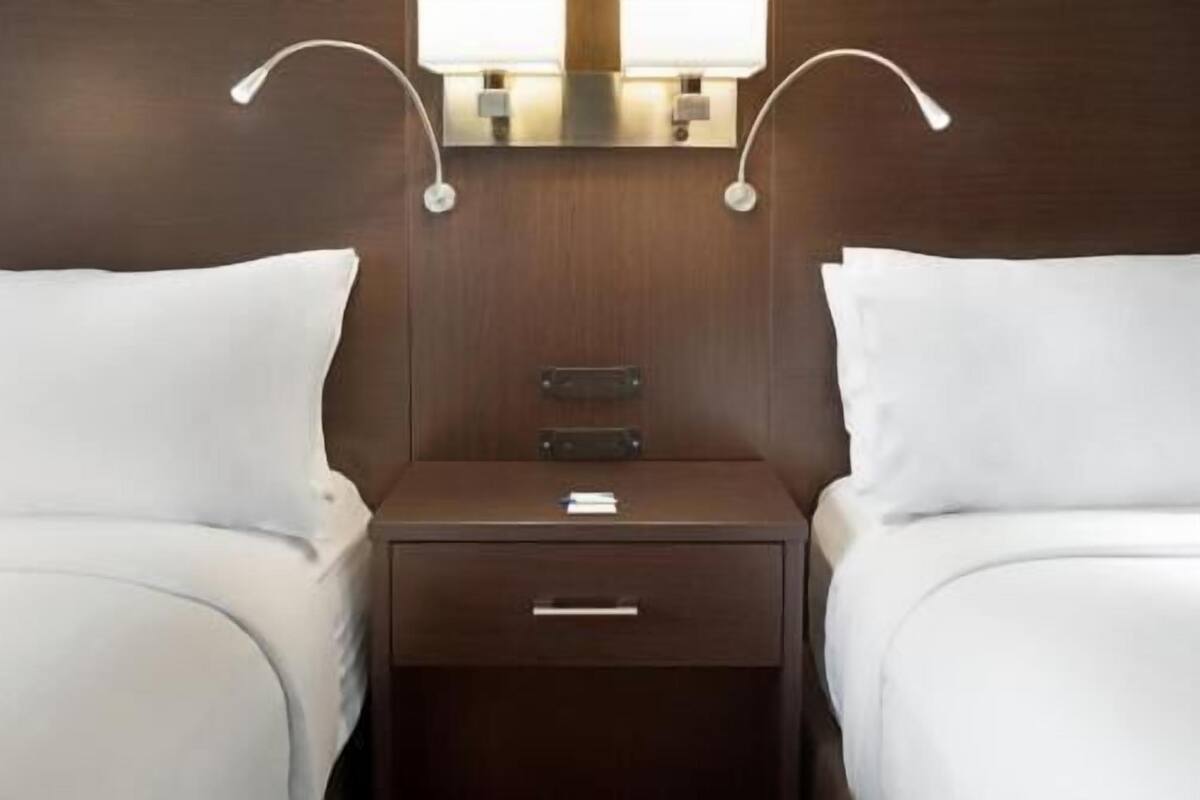 A hotel room with two beds, a nightstand with a drawer, and two wall-mounted lamps.