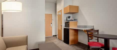 A hotel room with a sofa, a small table, a kitchen area with a microwave, and a dining table with chairs.