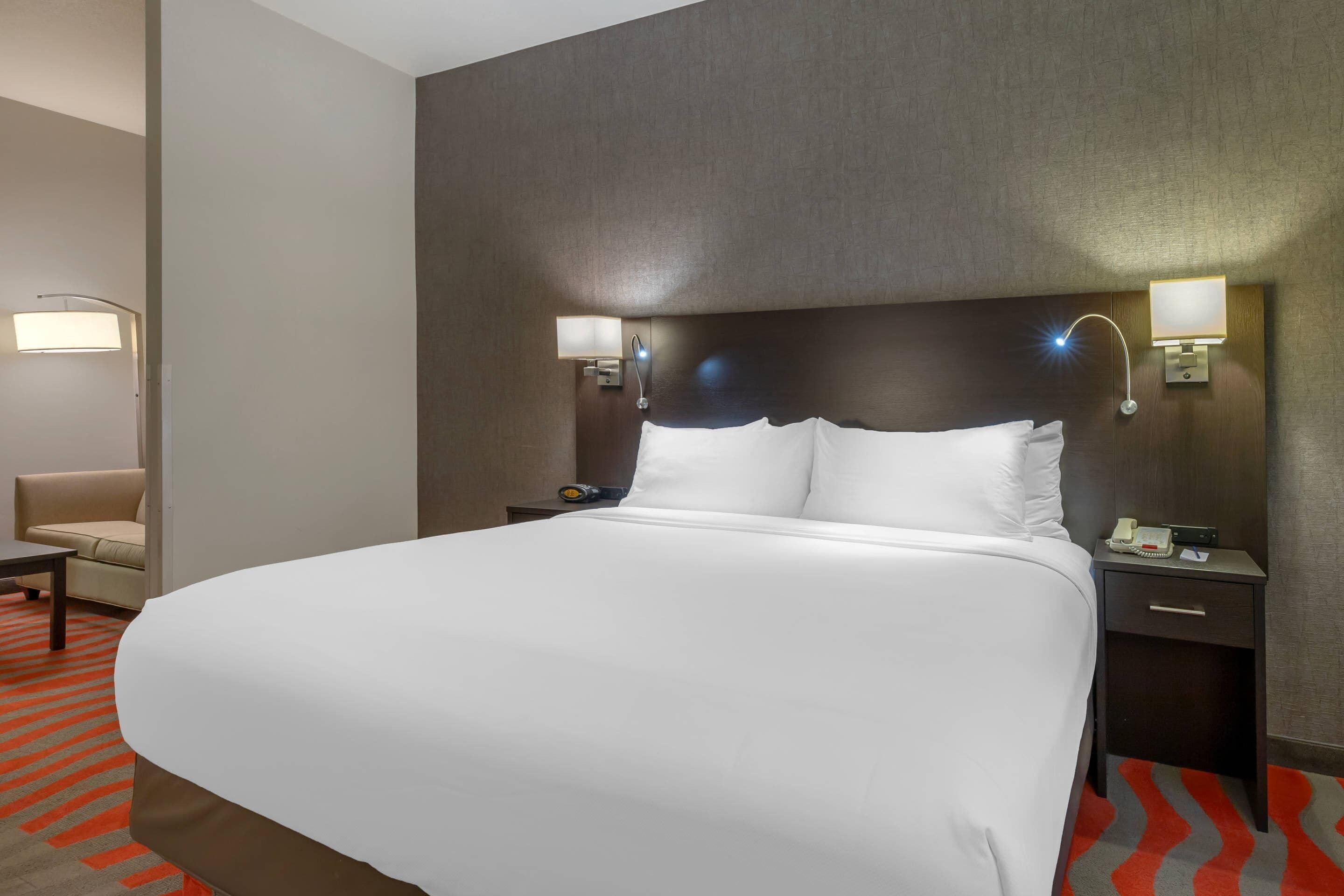 A hotel room with a large bed, two bedside tables with lamps, a chair, and a patterned carpet.