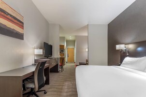 A hotel room with a bed, desk, chair, television, and a painting on the wall.