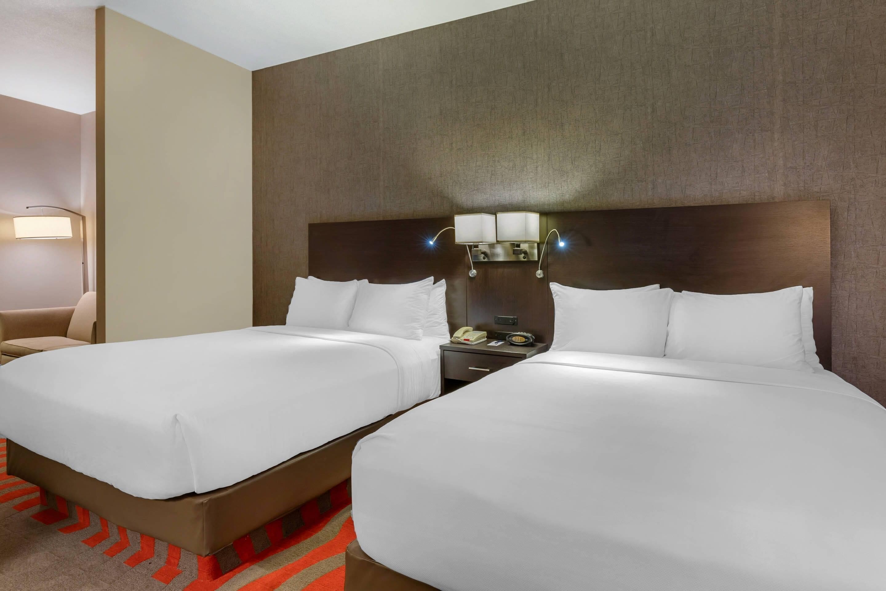 Ein Hotelzimmer mit zwei Betten, einem Nachttisch, einer Lampe und einem Sessel.