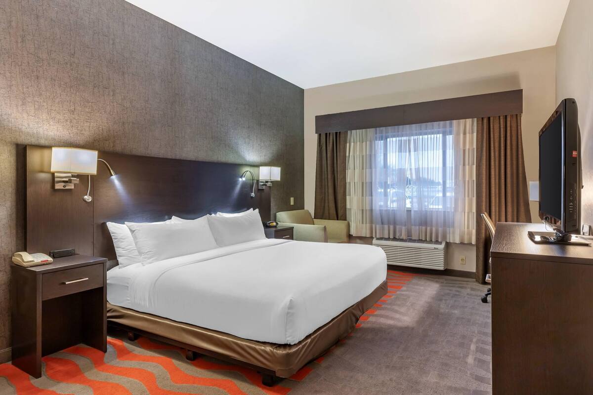 A hotel room with a large bed, bedside lamps, a desk with a computer, a chair, and a window with curtains.