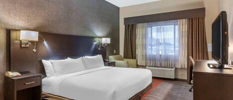 Una habitación de hotel con una cama grande, lámparas de noche, un escritorio con computadora, una silla y una ventana con cortinas.