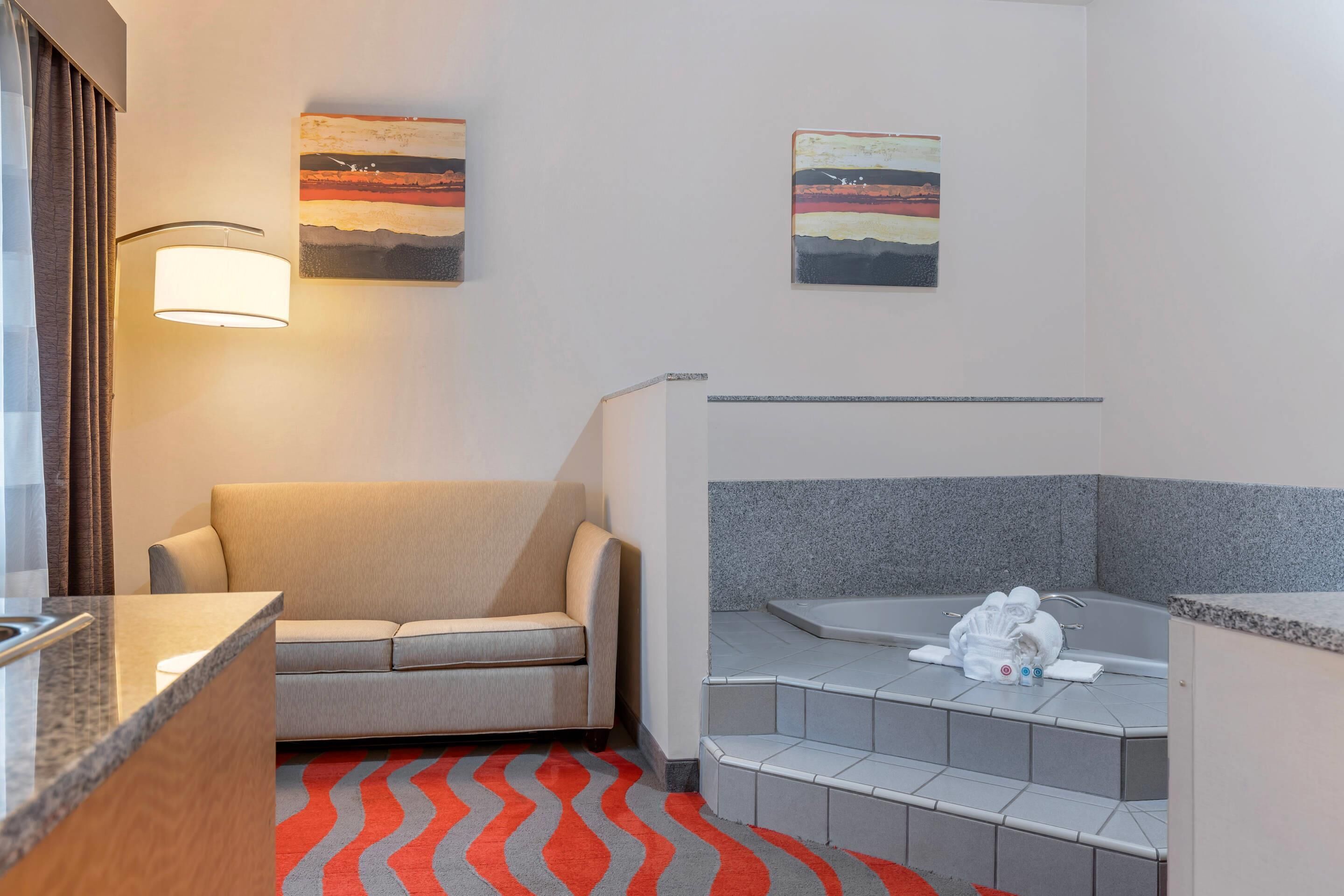 A hotel room with a sofa, a small table, a shower area, and two wall-mounted paintings.