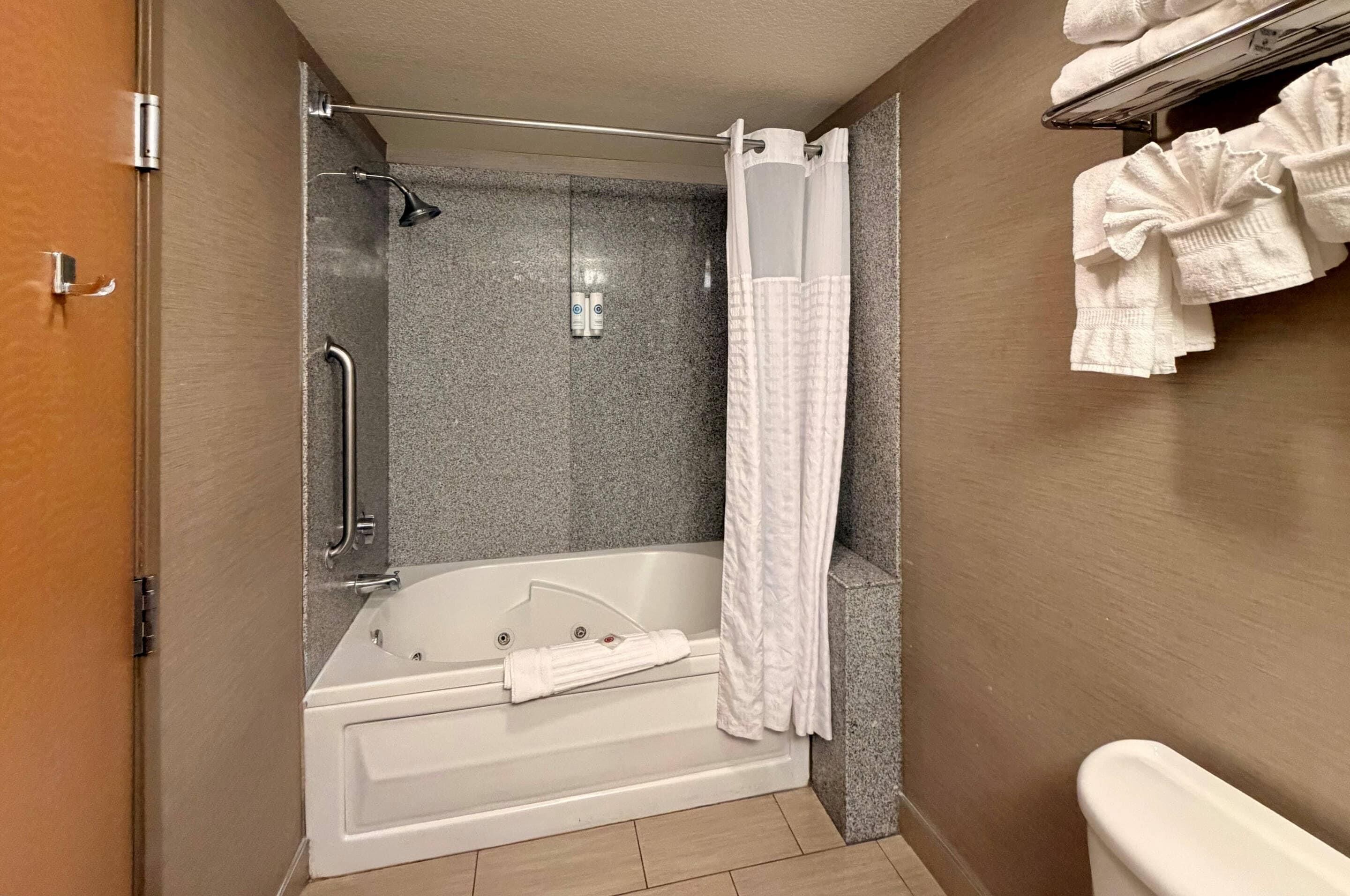 A bathroom with a bathtub, shower, and handrails.