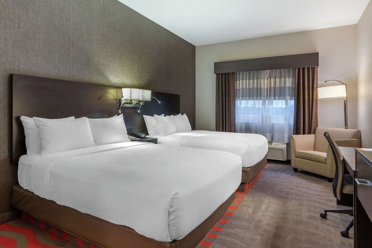 A hotel room with two beds, a desk, a chair, and a large window with curtains.