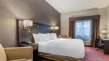 A hotel room with a bed, a desk, a chair, a lamp, and a window with curtains.