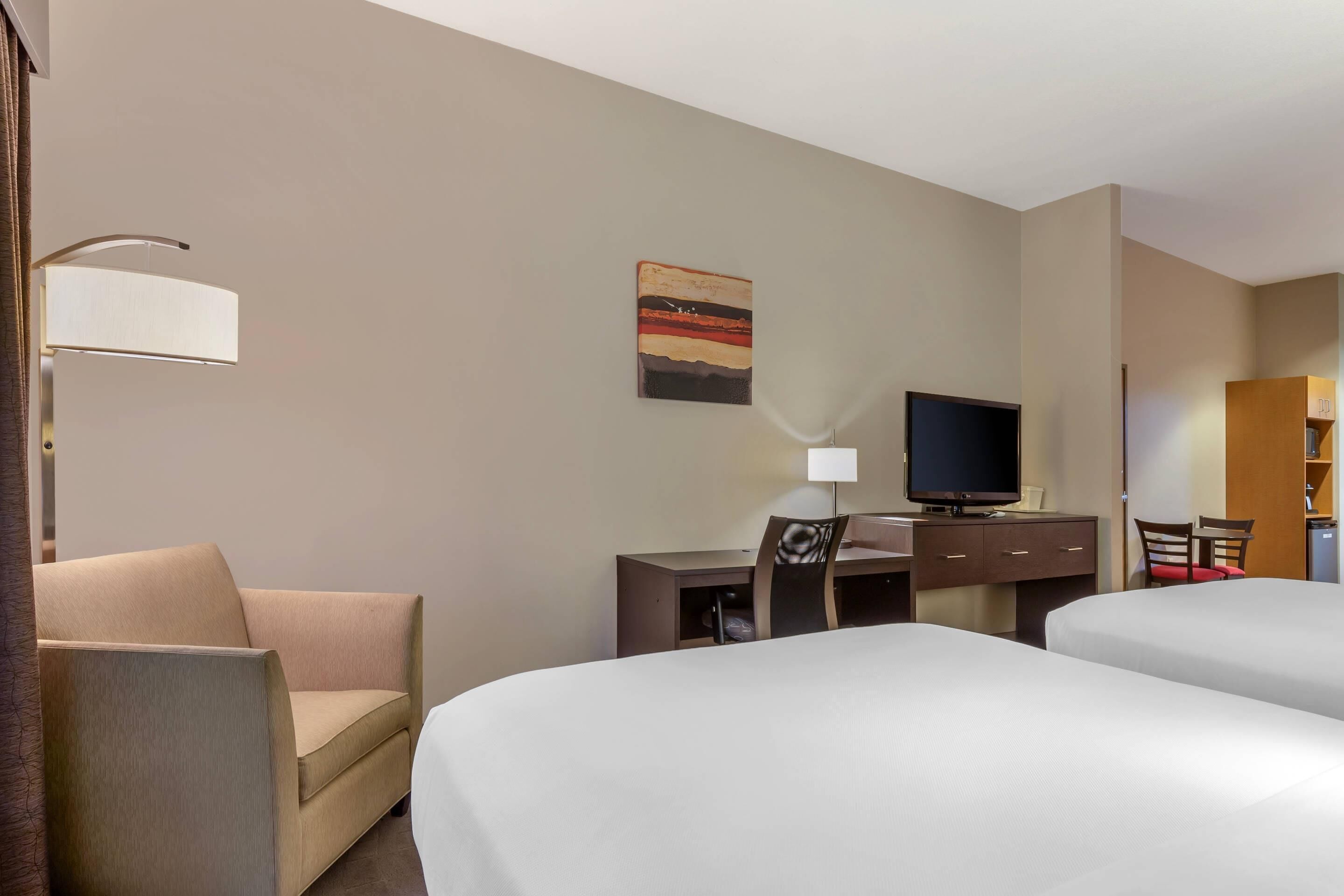 A hotel room with two beds, a desk with a chair, a television, and a painting on the wall.