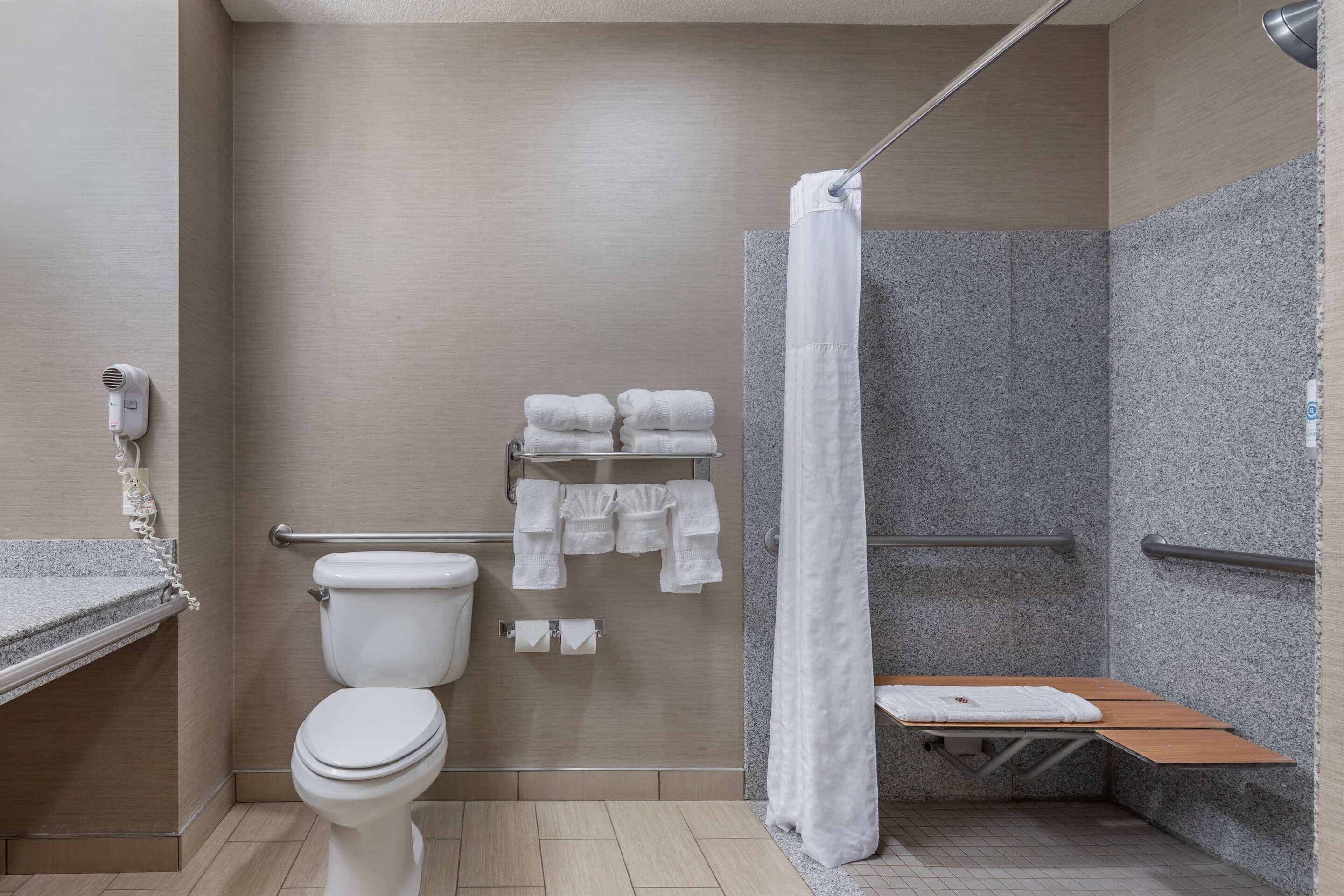 A modern bathroom with a toilet, shower, and a bench.