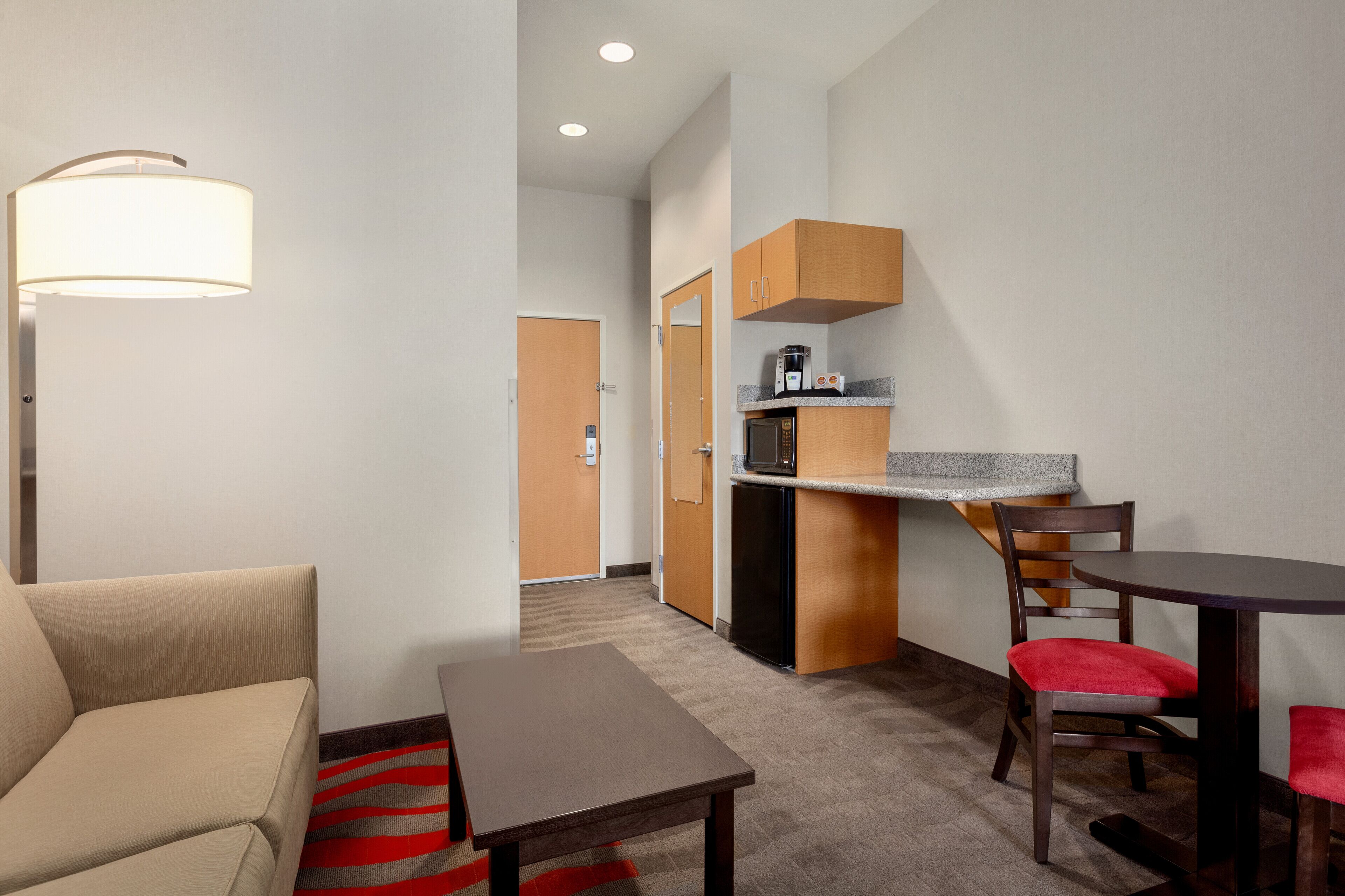 A compact hotel room with a sofa, a small table, a kitchenette, and a dining area.