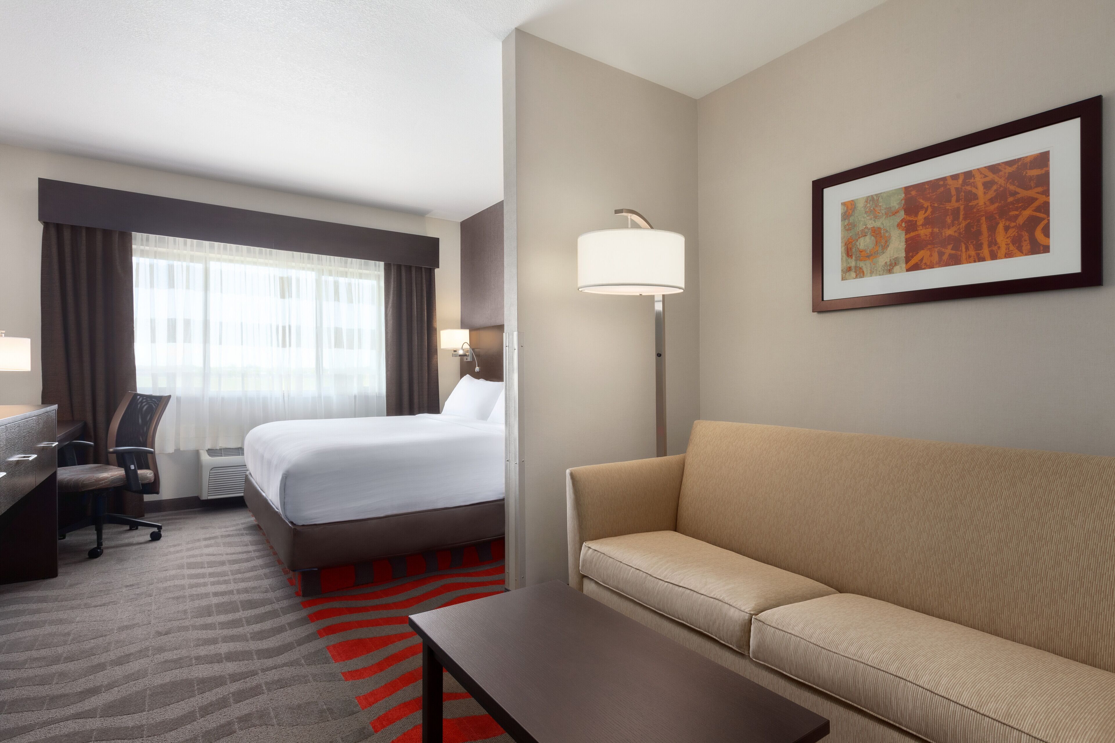 Een hotelkamer met een bed, een bank, een bureau, een stoel, een lamp en een lijst aan de muur.
