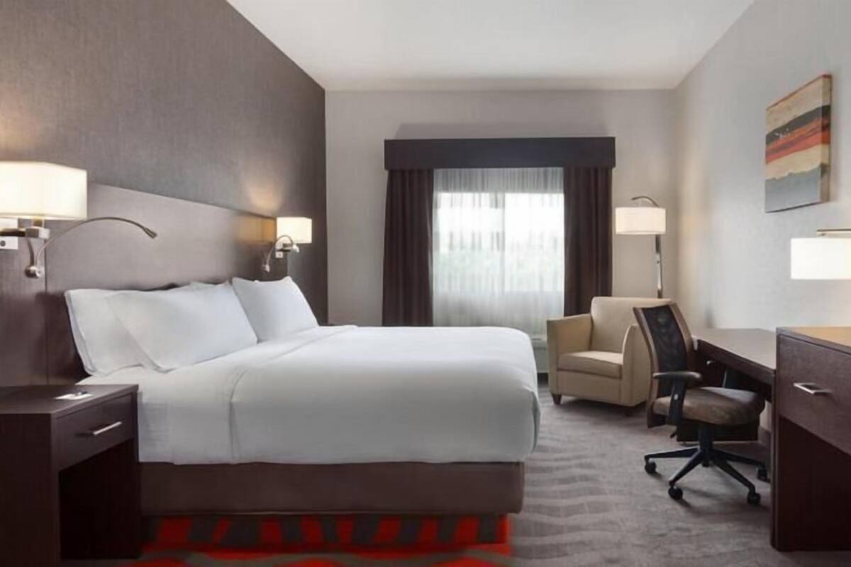 A hotel room with a bed, a desk, a chair, a television, and a window with curtains.