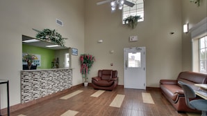A reception area with a reception desk, a brown leather chair, a brown leather sofa, and a computer desk with a chair. - Key West Inn - Millbrook (Millbrook)