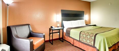 A hotel room with a single bed, a chair, a table with a phone, and a lamp.