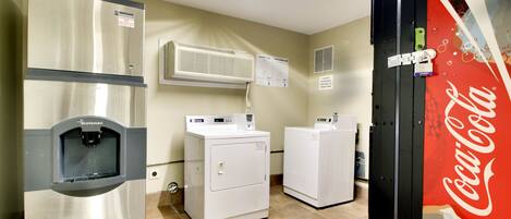 Un cuarto de lavado con un refrigerador de acero inoxidable, dos lavadoras blancas y un equipo de aire acondicionado.