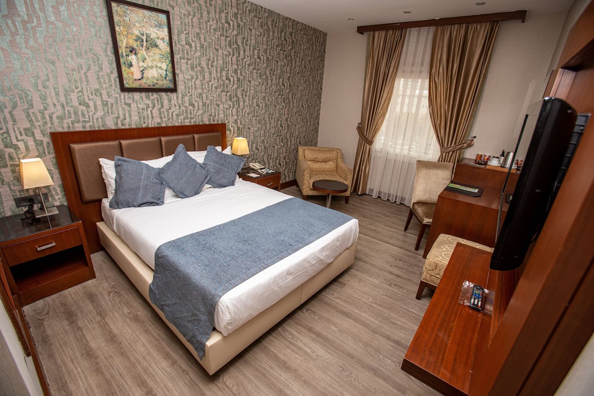 A hotel room with a large bed, a chair, a desk, a TV, and a nightstand with a lamp.