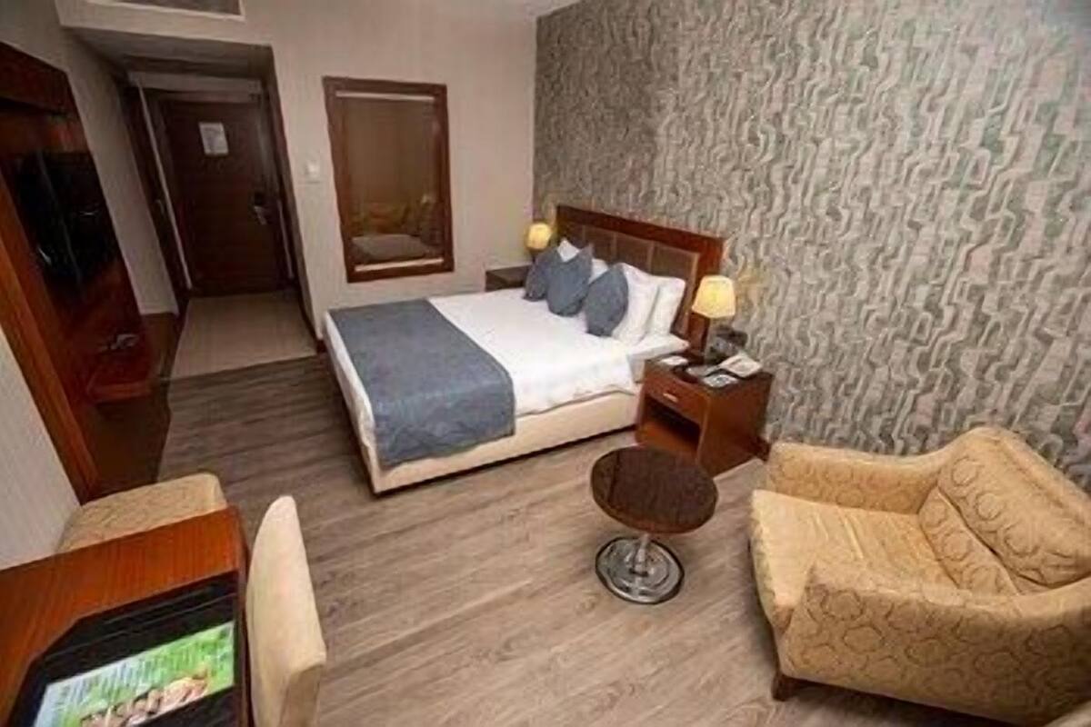 A hotel room with a bed, bedside table, lamp, chair, and a television.