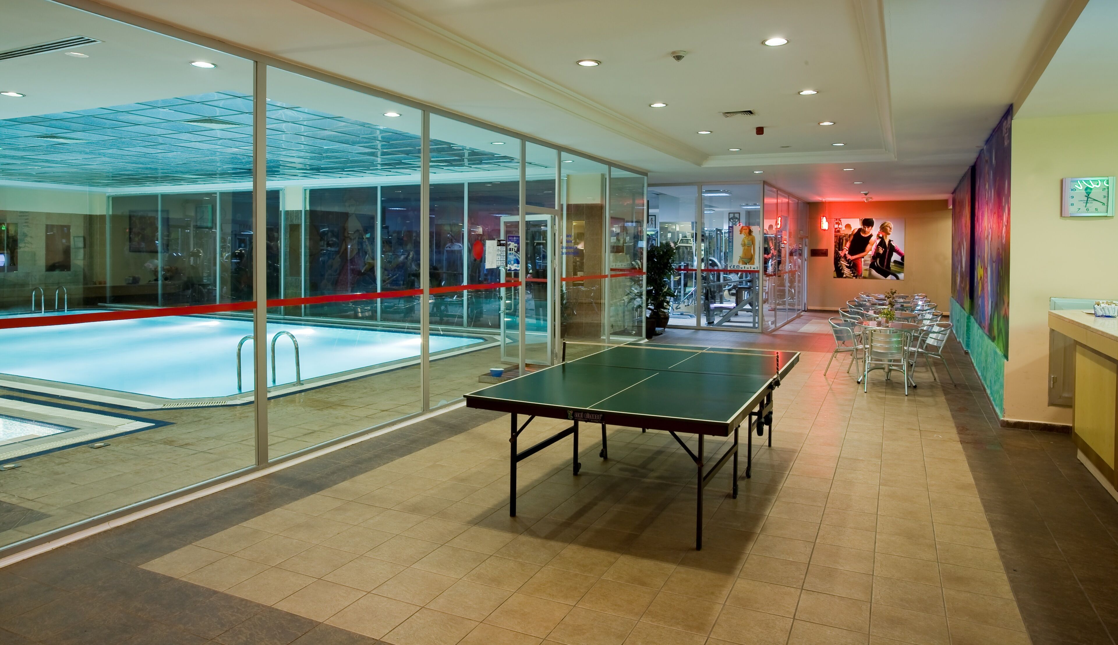 Un espacio interior amplio con mesa de ping pong, piscina cubierta y zona de estar con sillas y mesas.