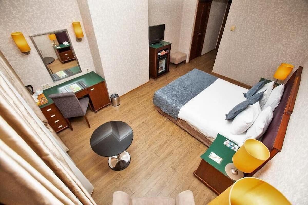 A hotel room with a bed, desk, chair, and a small table with a lamp.