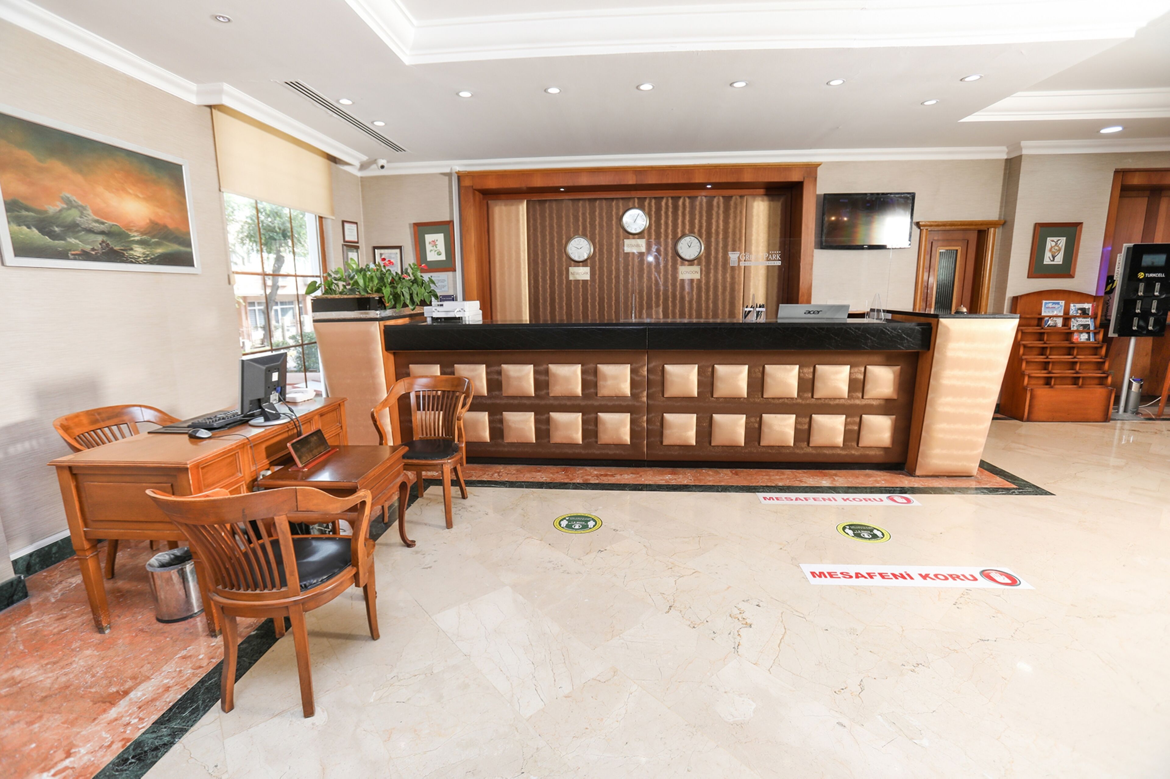 A hotel reception area with a wooden reception desk, a seating area with chairs, and a large painting on the wall.