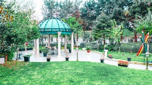 Un belvédère surmonté d’un toit végétalisé, entouré d’un jardin bien entretenu où poussent différentes espèces de plantes et où s’étend une pelouse.
