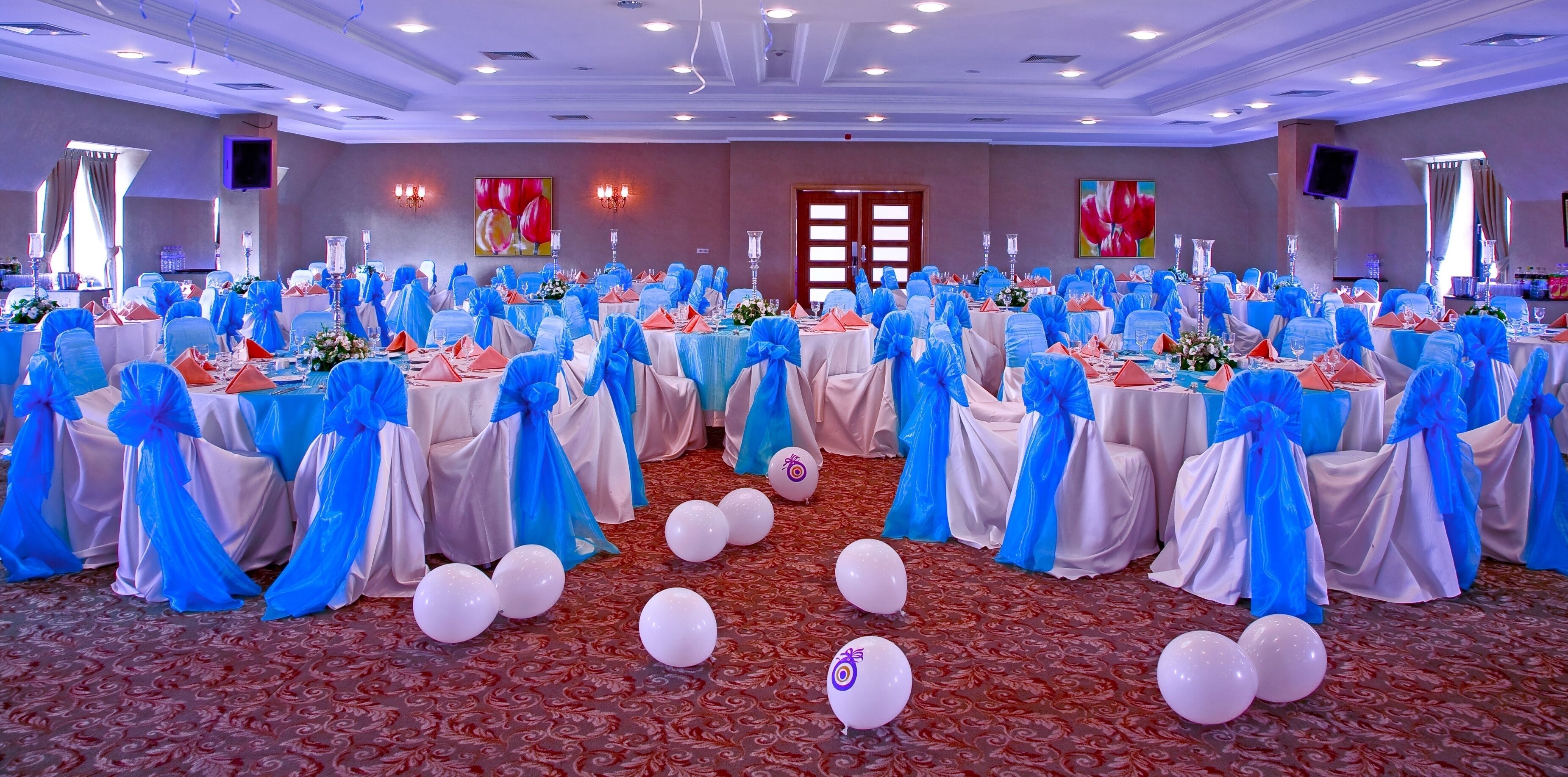 A banquet hall with round tables covered in white tablecloths and blue sashes, arranged in rows.