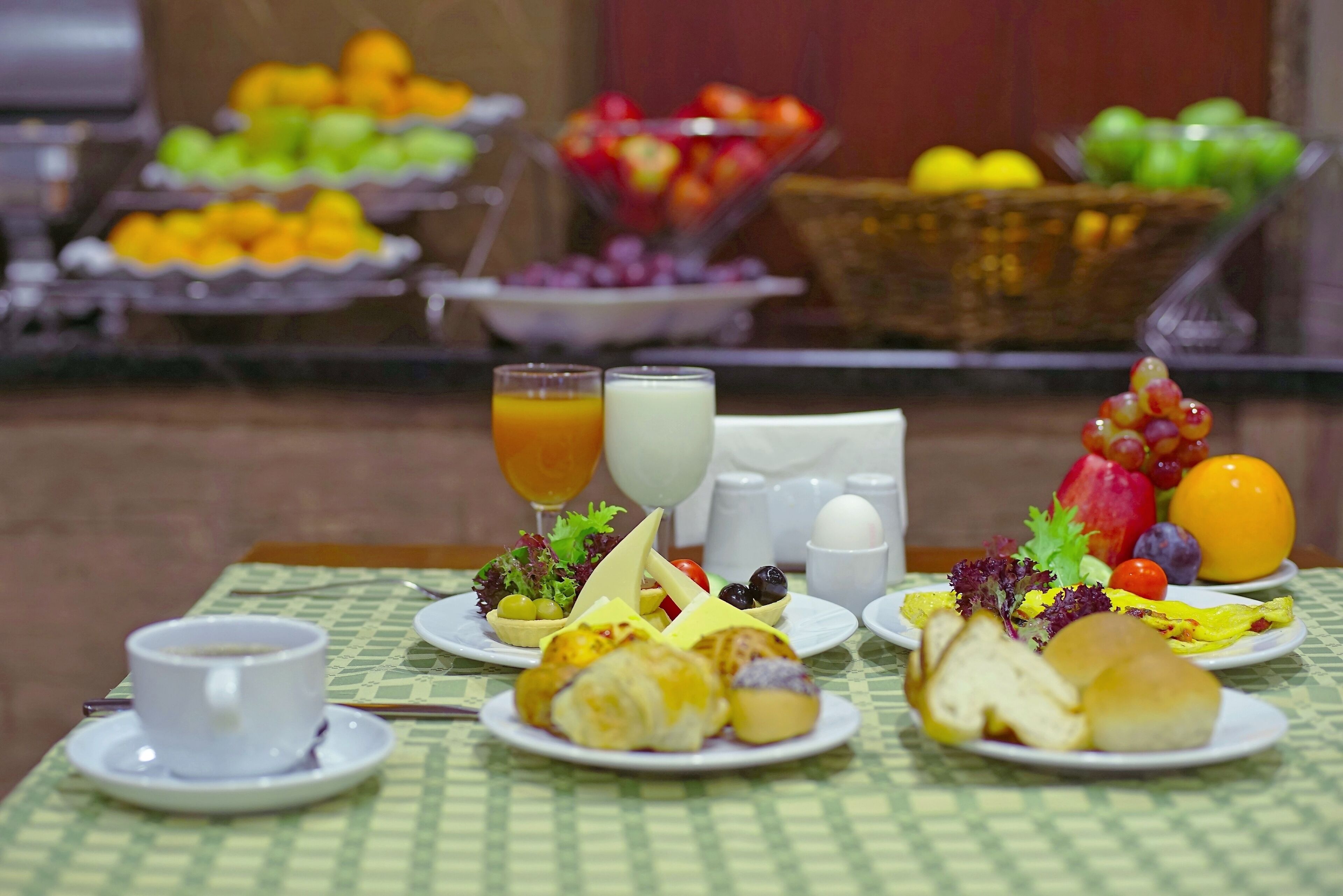 Ein Frühstücksbuffet mit verschiedenen Früchten, Gemüsesorten und Backwaren auf einer karierten Tischdecke.