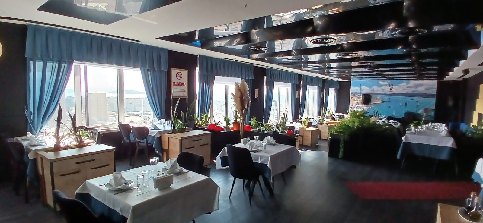 Ein Restaurant mit mehreren Tischen, blauen Vorhängen und Blick auf die Stadt.