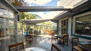 An outdoor patio area with tables and chairs, glass walls, and a view of a building in the background. - The Green Park Bostancı (Istanbul)
