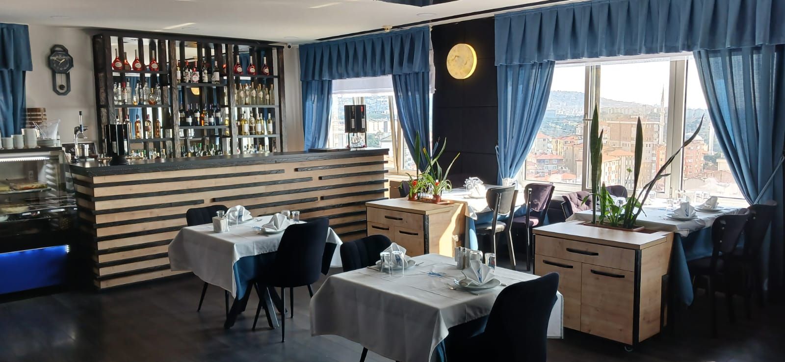 A restaurant with a bar area, tables set for dining, and a view of the city through large windows.
