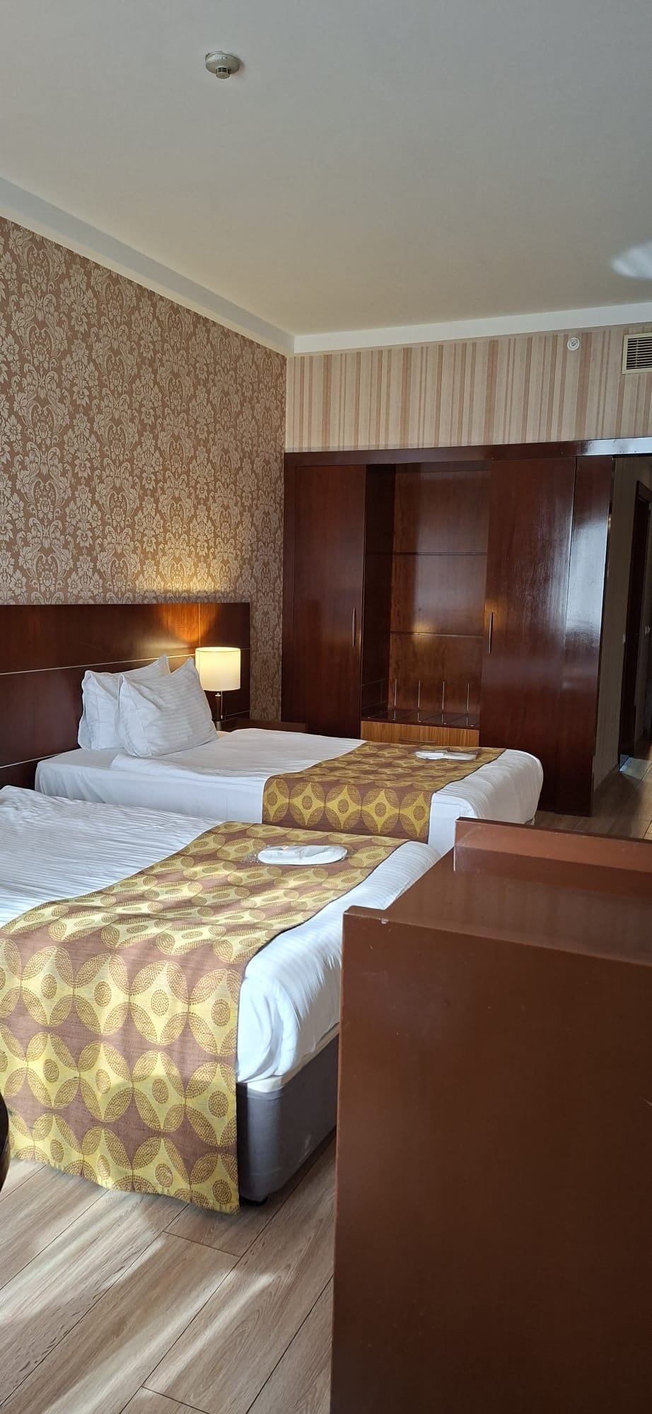 A hotel room with two beds, a large wardrobe, and a patterned wall.