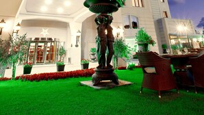 A hotel with a tall, white building, a well-lit entrance, and a garden area with a statue and chairs. - The Green Park Bostancı (Istanbul)