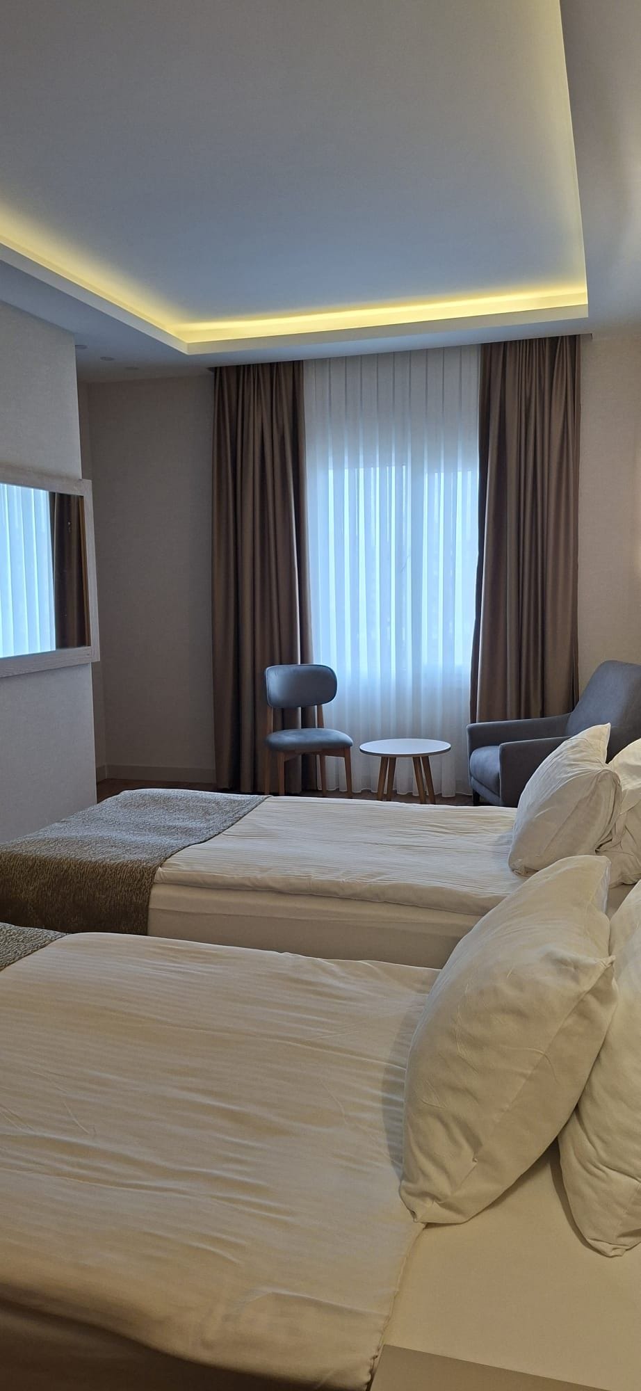 Une chambre d’hôtel avec deux lits, une petite table, une chaise et une fenêtre avec des rideaux.
