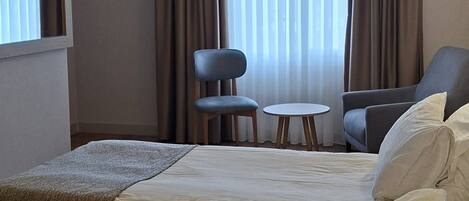 Une chambre d’hôtel avec deux lits, une petite table, une chaise et une fenêtre avec des rideaux.