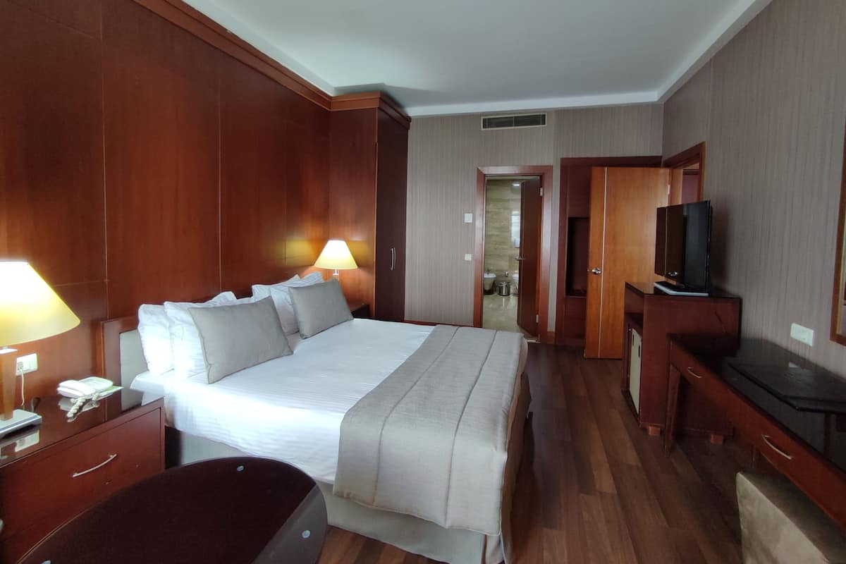 Quarto de hotel com uma cama grande, abajures, uma escrivaninha com televisão e um guarda-roupa.