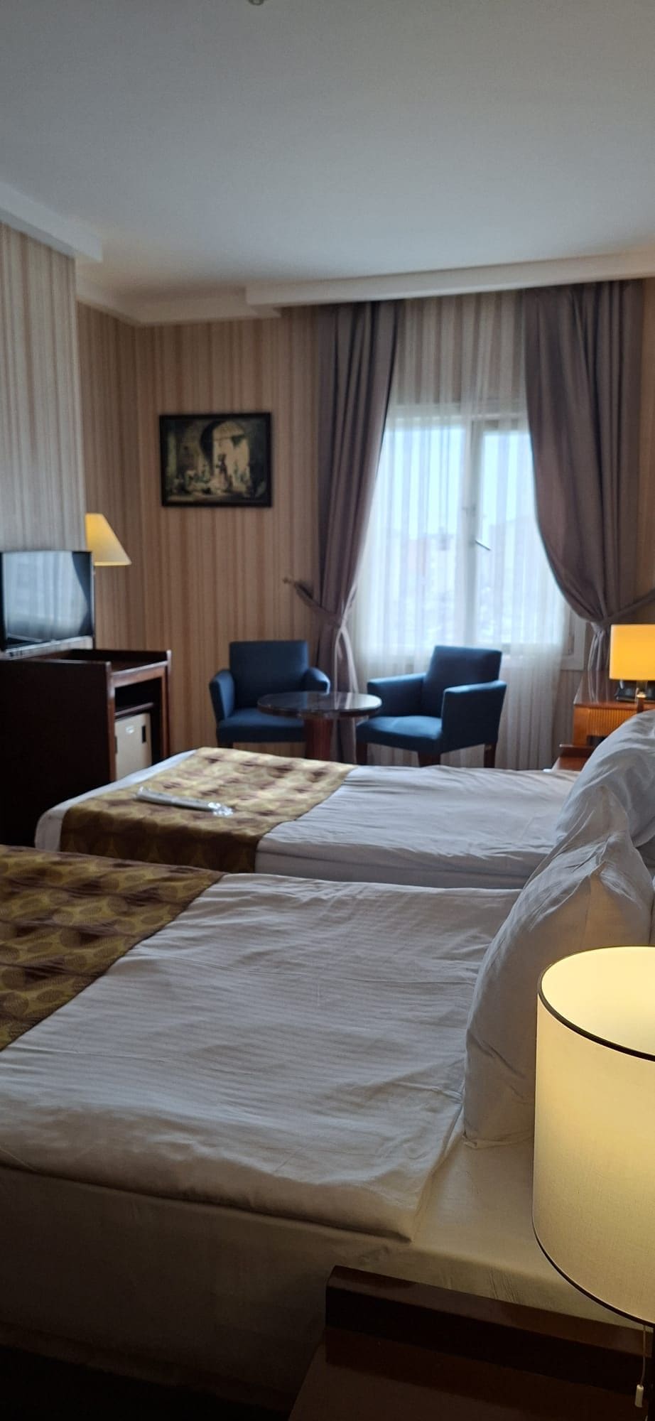 A hotel room with two beds, a desk with a lamp, a chair, and a television.