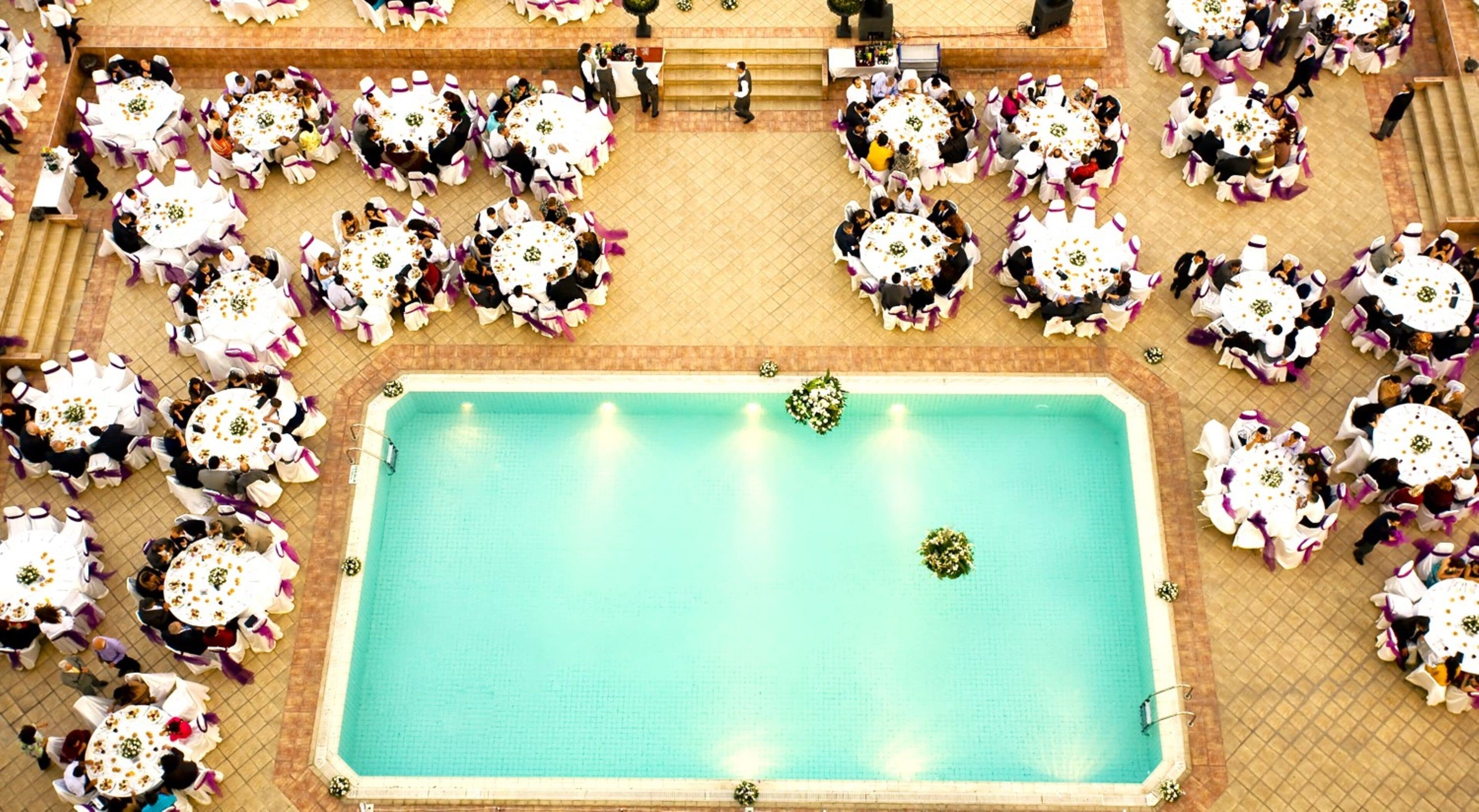 An aerial view of a pool area with multiple round tables and chairs, arranged in a circular pattern around the pool.