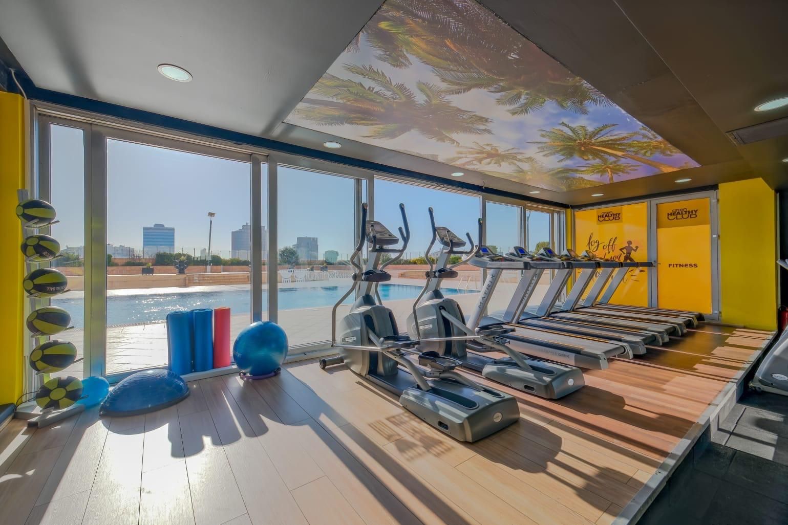 Une salle de sport équipée de matériel d’exercice, une piscine et une vue sur la ville.