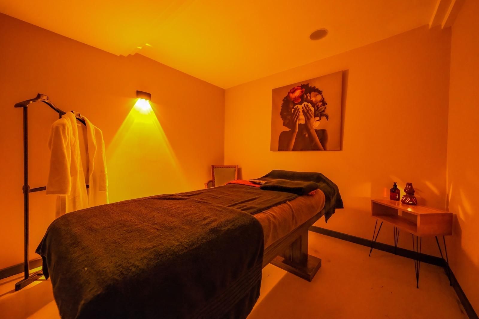 A room with a bed, a chair, a table with items, and a wall-mounted light.