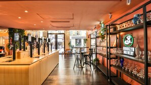 Uma área de bar com um balcão comprido, banquetas e prateleiras com copos.