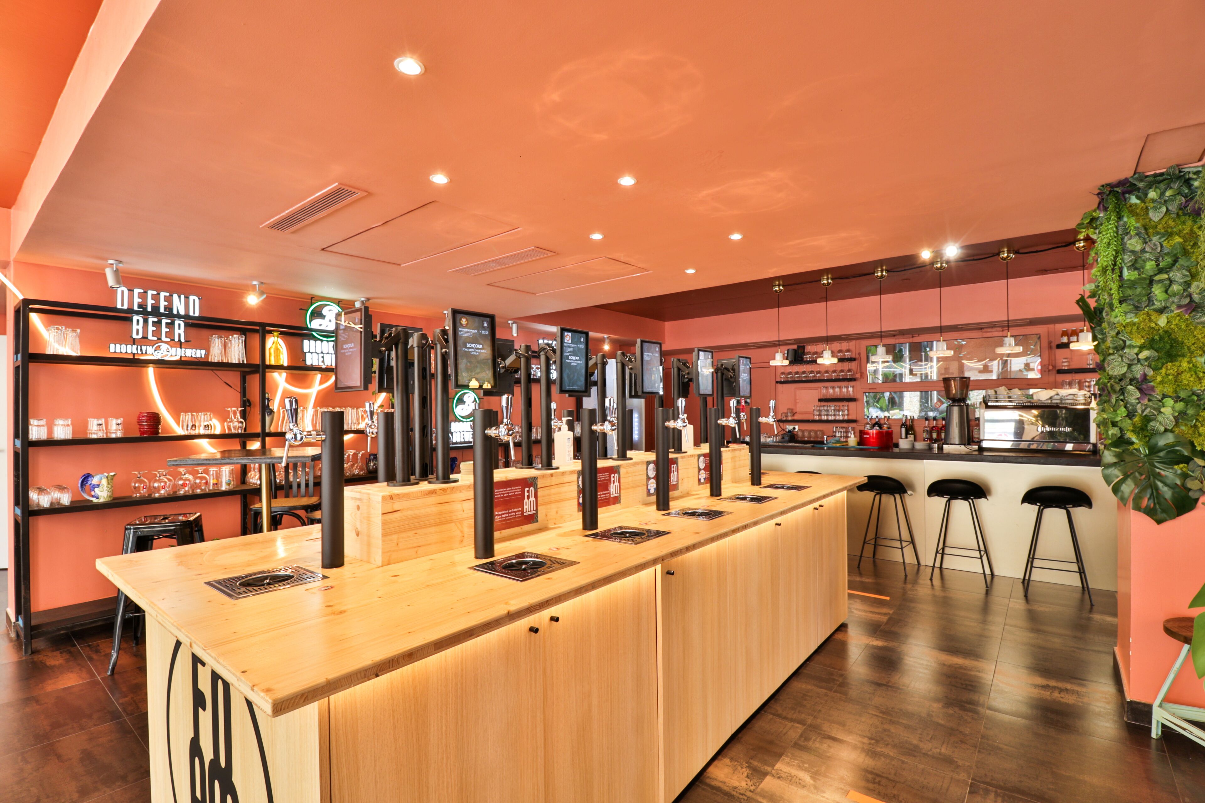A bar area with a long counter, multiple taps, and a shelf with various bottles.