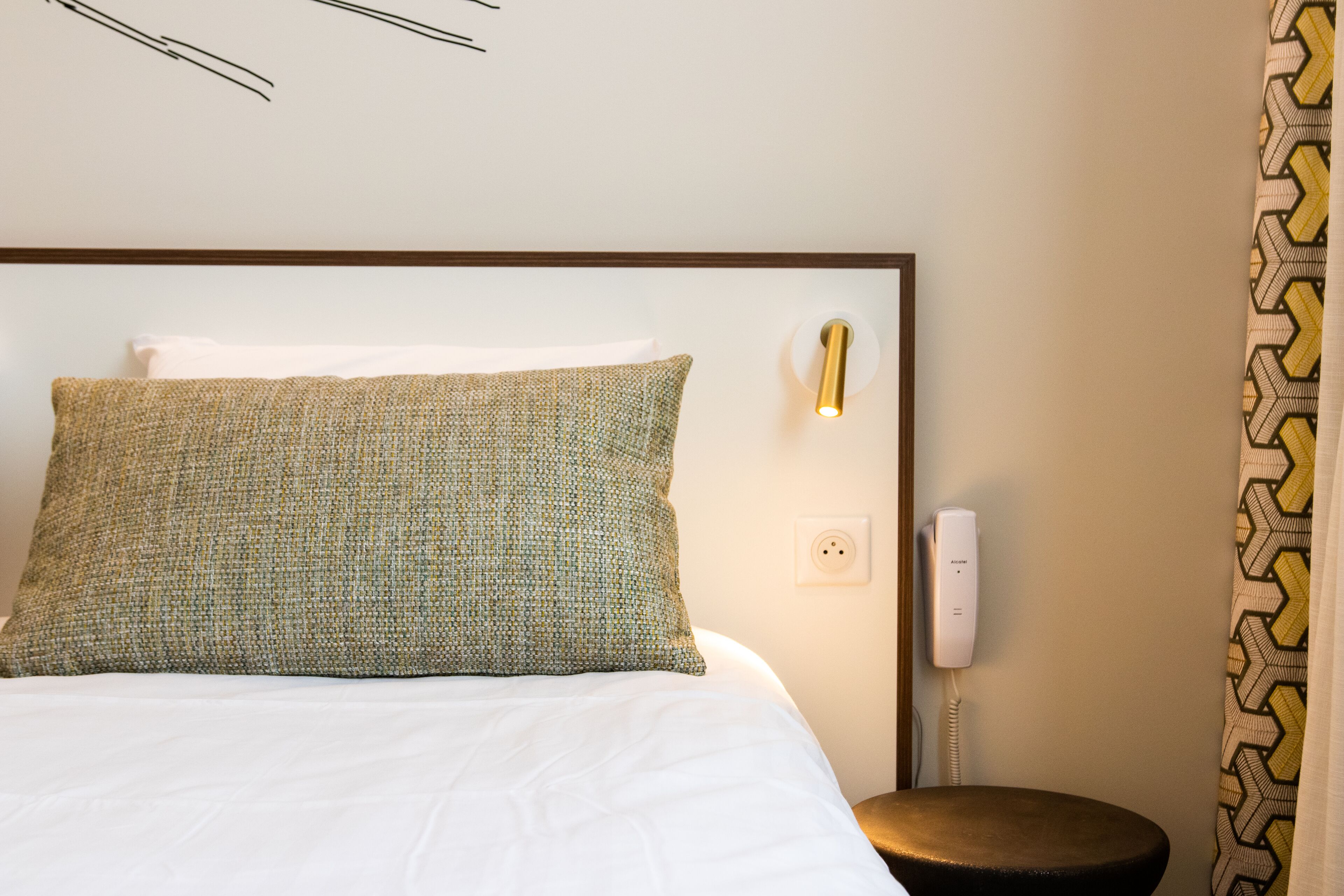Una habitación de hotel con una cama, una mesita de noche, un teléfono y una cortina estampada.