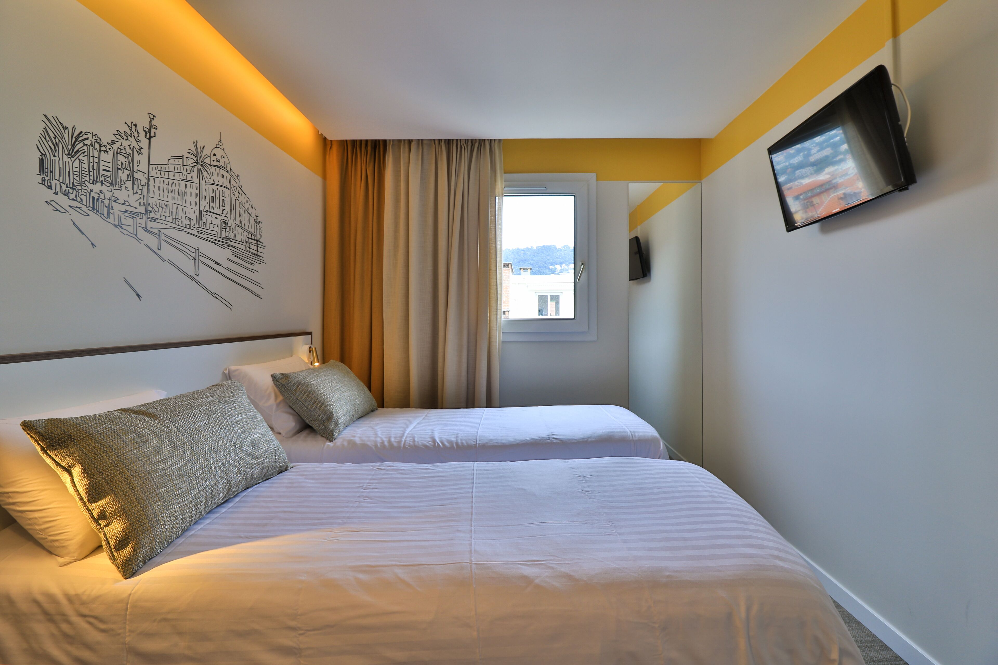 A hotel room with two beds, a window, a wall-mounted TV, and a cityscape mural.