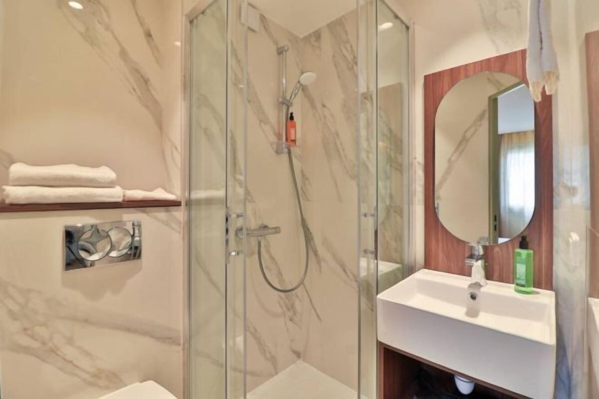 A modern bathroom with a glass-enclosed shower, a white sink, and a large mirror.